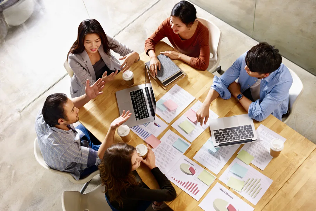 A team collaborating around a table with laptops, notes, and workshop materials